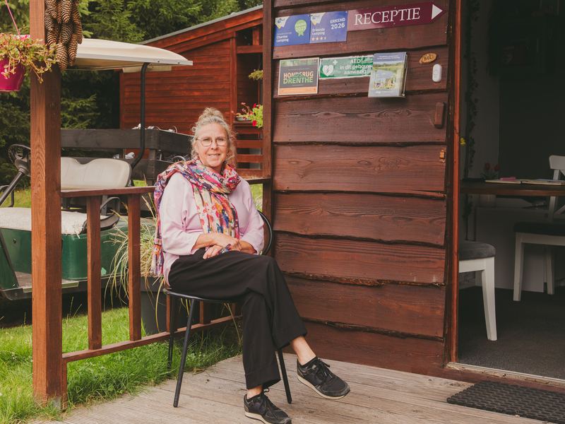 Glimlachende gastvrouw op een stoel naast de open deur van de receptie op Landgoed Tolhek